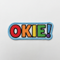 Embroidered iron-on patch with OKIE in bold rainbow colored letters, clean cheerful style